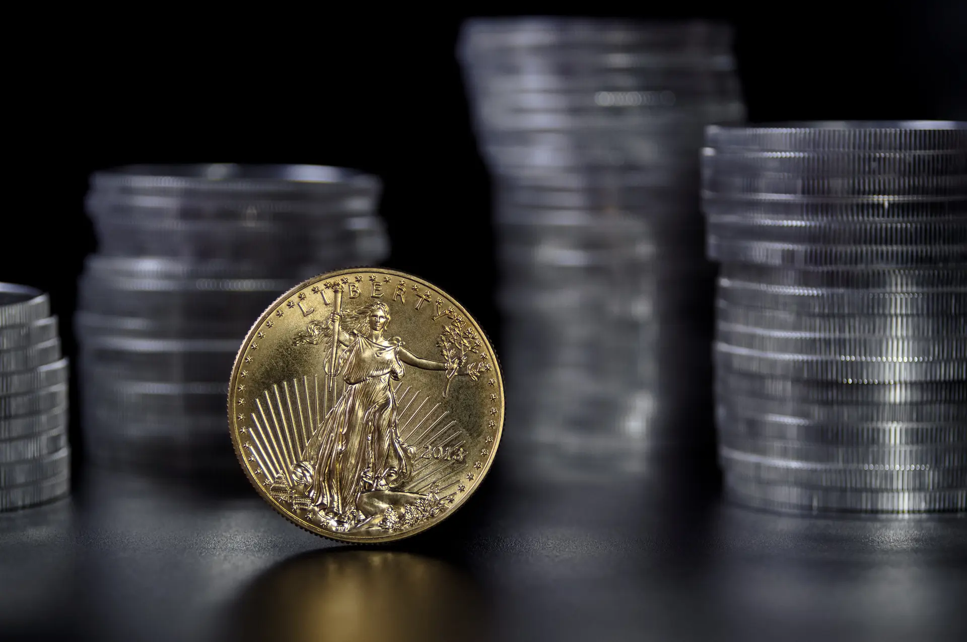 1 oz American Gold Eagle coin in front of stacks of Silver Eagle coins